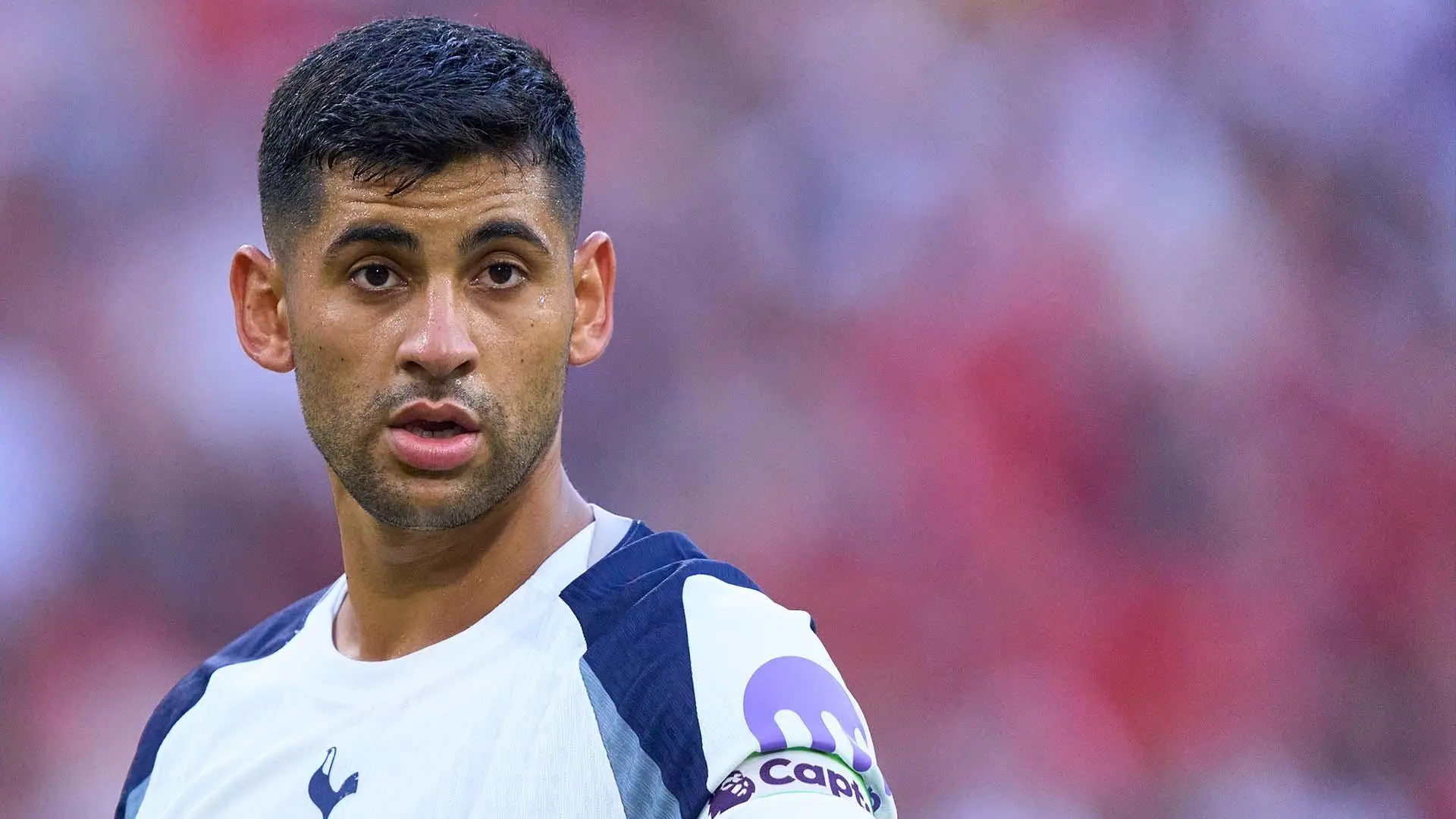 Close-up of Cristian Romero wearing a Tottenham Hotspur white and navy kit with a captain's armband