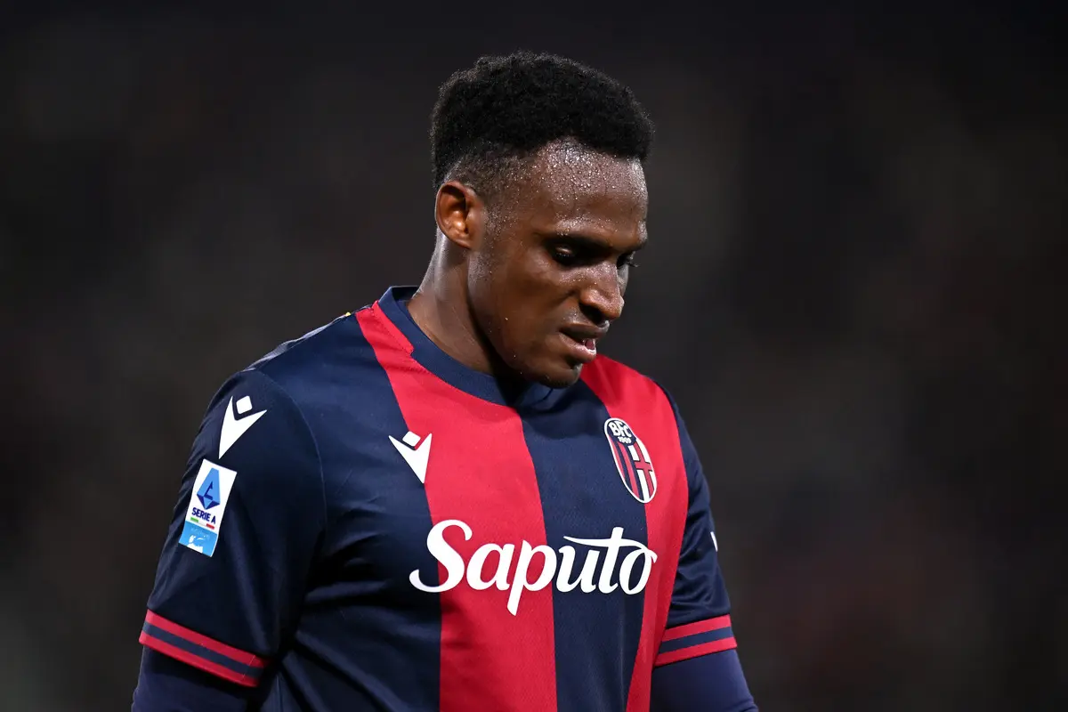Football player wearing Bologna FC jersey, looking down on the field.