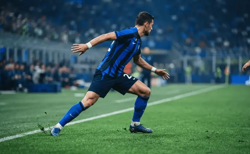 Football defender in blue and black stripes positioned tactically on stadium pitch with dramatic lighting