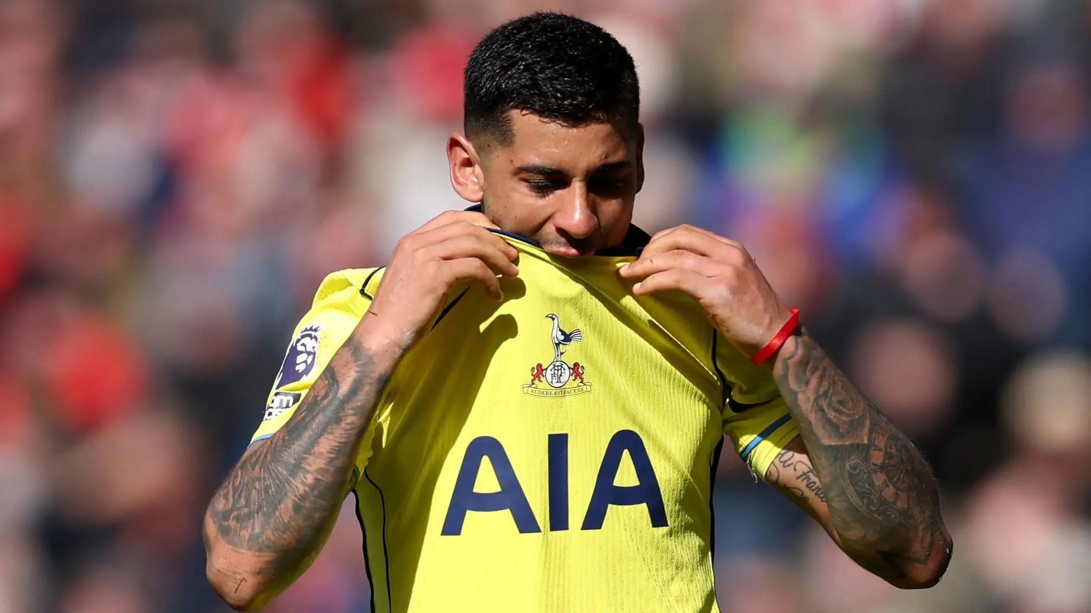 Cristian Romero wearing a yellow Tottenham Hotspur jersey and holding the club crest