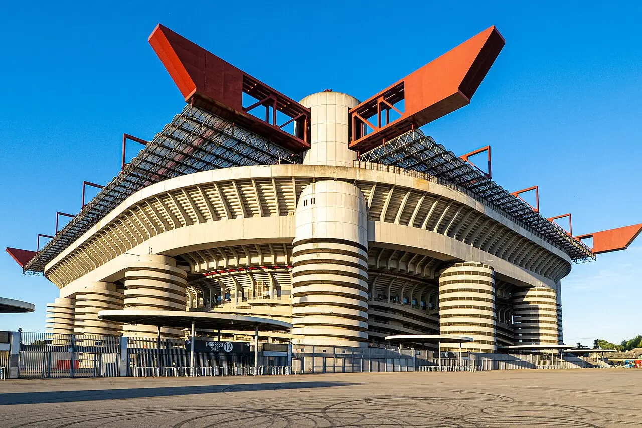 Exterior view of the San Siro stadium in Milan, featuring its distinctive red roof supports and concrete pillars