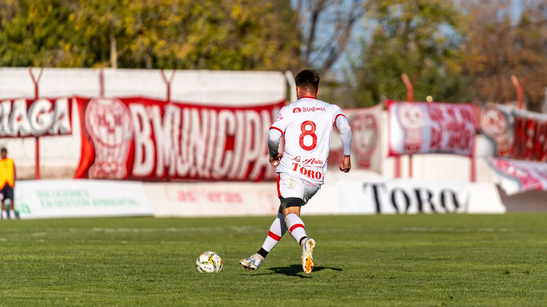 Rear view of a soccer player wearing a white jersey with the number 8, running toward a ball on a grass field.