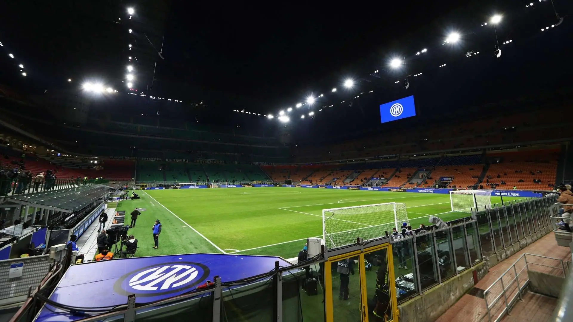 Wide view of San Siro stadium at night with Inter Milan logos on the screen and field equipment.