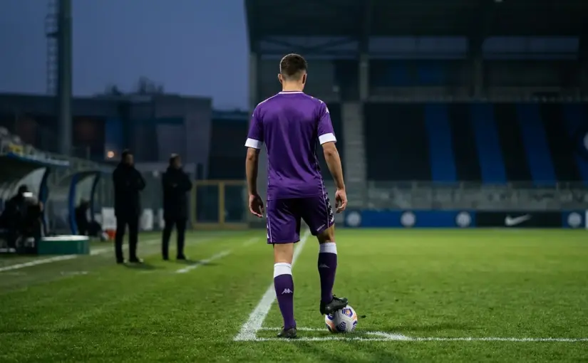 Young midfielder viewed from behind on a floodlit pitch as Inter and Juventus monitor his Fiorentina future