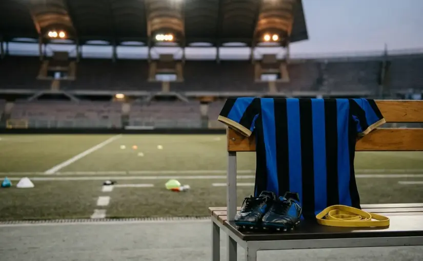 Inter-inspired football shirt and boots beside a floodlit pitch representing Calhanoglu's midfield absence