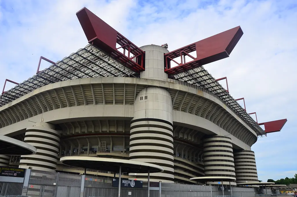 External view of the San Siro stadium in Milan showing its distinctive architecture and red roof structures.